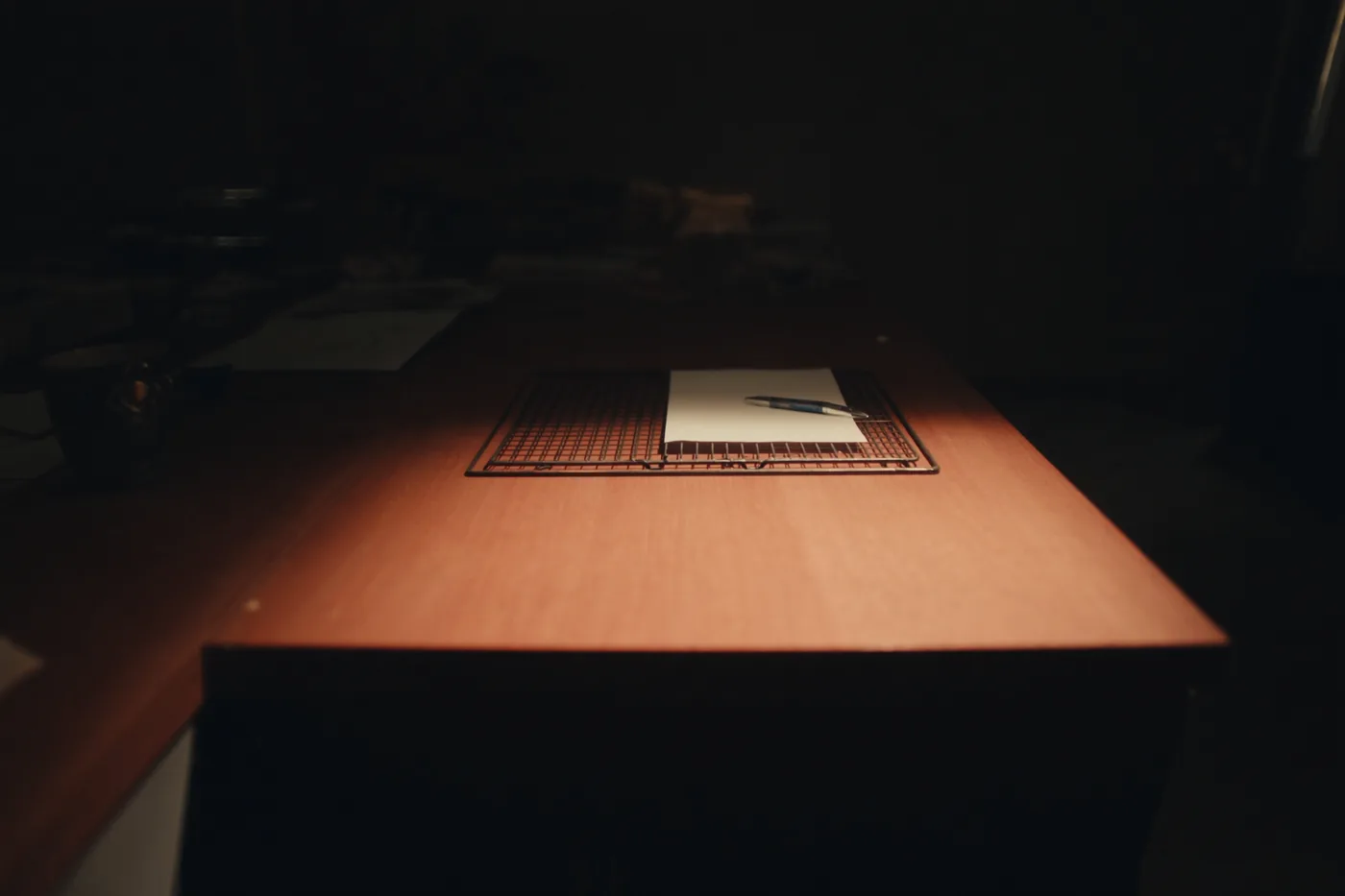 An overhead view of a single sheet of paper in a wire inbox tray on a wooden desk, a pen laid across it.
